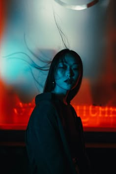 a woman standing in front of a neon sign with her hair blowing in the wind