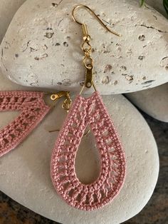 a pair of pink crocheted earrings sitting on top of a rock next to a plant