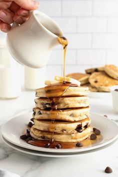 a stack of pancakes being drizzled with syrup and chocolate chips on the side