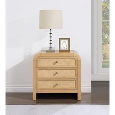 a nightstand with two drawers and a lamp on it in front of a white wall