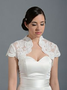 a woman in a white dress with a lace jacket on her shoulders and neckline