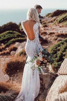 a woman standing on top of a rocky hillside wearing a white dress and holding a bouquet