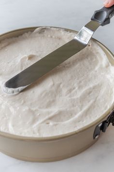 a person using a knife to cut into a cake in a pan with white frosting