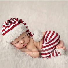 a newborn baby wearing a red and white striped hat with pom - poms