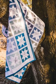 two quilts are hanging from a tree in the woods, one is blue and white