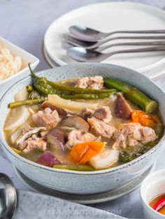 a bowl of soup with meat, vegetables and rice on a table next to silverware