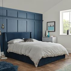 a bed with blue headboard in a bedroom next to a window and wooden floor