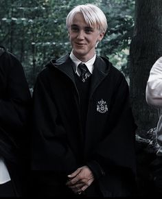 two young men dressed in harry potter robes standing next to each other with trees in the background