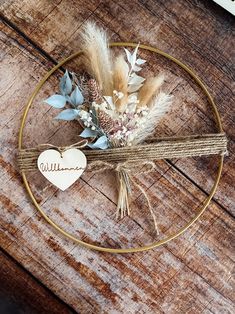 an arrangement of dried flowers and feathers on a wooden table with a heart shaped ornament