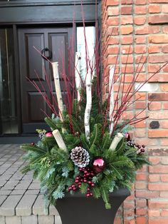 a potted plant with red berries, pine cones and greenery in front of a brick building