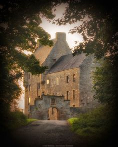 an old stone building with trees around it and a path leading up to the entrance