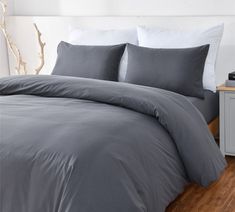 a bed with grey sheets and pillows on top of wooden flooring next to a white wall