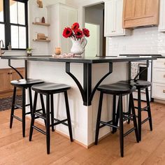 a kitchen island with three stools and a vase filled with red flowers on it