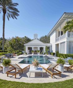 an outdoor pool surrounded by lawn chairs and potted plants with palm trees in the background