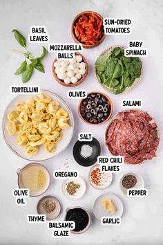 the ingredients for an italian pasta dish laid out on a white counter top, including basil leaves, mozzarella shells, olives, orecchini and red sauce