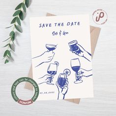 save the date card with hand holding wine glasses and green leaves next to it on a table