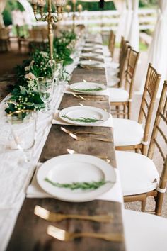 the table is set with white plates and greenery