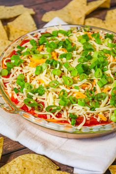 a glass dish filled with cheese and veggies next to tortilla chips