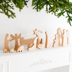 wooden nativity figurines sitting on top of a mantel with pine branches