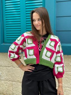 a woman standing in front of a blue wall wearing a pink and green knitted sweater