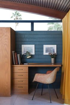 a desk with a chair next to it in front of a window and yellow curtains