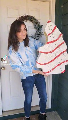 a woman is holding up a large piece of cake in front of a door with a wreath on it