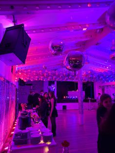 people are standing in a room with purple lights and balloons on the ceiling, while one person is taking a photo