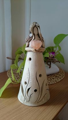 a white vase sitting on top of a wooden table next to a potted plant