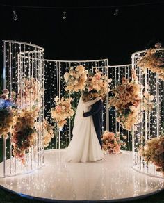 a bride and groom standing in front of an arch with flowers on it at night