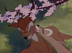 two deer standing next to each other under a tree with pink flowers on its head