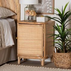 a wicker cabinet next to a bed with a lamp on top and a plant in the corner