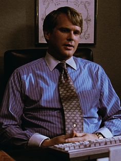 a man sitting in front of a computer keyboard wearing a tie and dress shirt with his hands on the keyboard