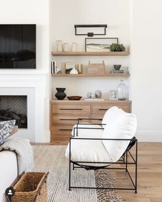 a living room with a white couch, chair and television on a shelf above the fireplace