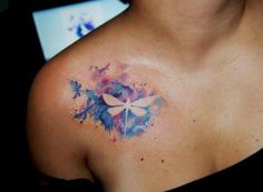 a woman's chest with a dragonfly tattoo on her left shoulder and watercolor paint splatters all over it