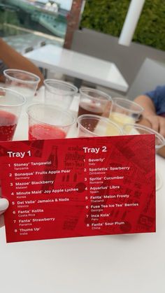 a person holding up a card with drinks in it on top of a white table