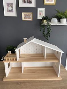 a doll house is shown with pictures on the wall behind it, and in front of a potted plant