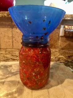 a jar filled with red sauce sitting on top of a counter next to a blue strainer