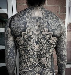 the back of a man with tattoos on his body, and a skull in the middle