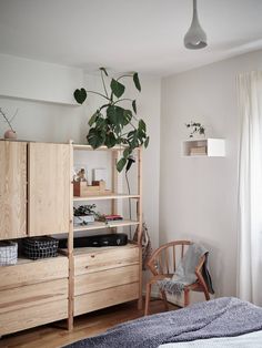 a bedroom with wooden furniture and plants on the shelves in front of the bed, next to a window