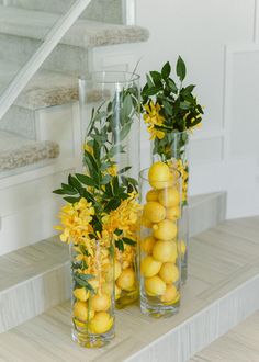 three tall vases filled with lemons and flowers