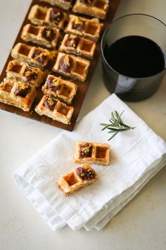 small waffles are sitting on a napkin next to a cup of coffee and a tray of cookies