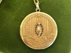 "Description: A large and lovely antique round Art Nouveau monogrammed gold filled photo locket on a new 14K gold filled chain.  The front of this locket made by the SB Company, features a central raised oval shape surrounded by a total of 14 \"paste\" stones. The stones that were probably once clear have darkened with age. There are 7 in paste gems on each side of the central oval. At the top and at the bottom of this oval shape is a raised fleur de lis. There are a total of 6 raised vertical l Heirloom Oval Link Locket Necklace, Ornate Oval Locket Necklace, Antique Engraved Oval Locket Necklace, Victorian Antique Gold Oval Locket Necklace, Victorian Oval Brass Locket Necklace, Round Art, Photo Locket, Antique Art Deco, Gold Filled Chain