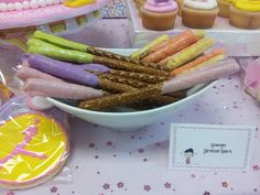 there is a bowl full of candy sticks on the table with cupcakes in the background