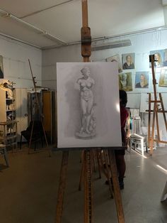 a woman standing in front of an easel with a drawing on it