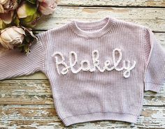 a pink sweater with the word bakey written on it next to some flowers