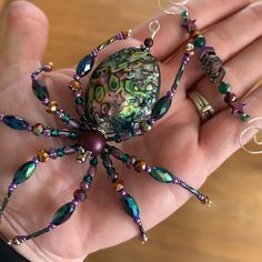 a hand holding a green and purple beaded spider on it's palm,