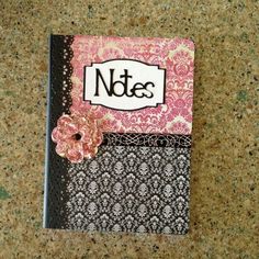 a note book with a pink flower on the front and black cover, sitting on a table