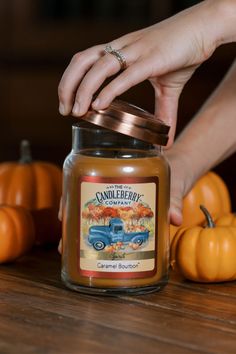 a person holding a candle in front of some pumpkins on a wooden counter top