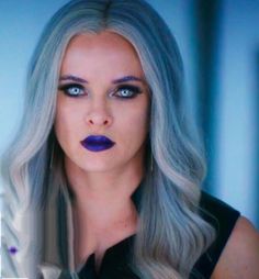 a woman with grey hair and blue eyes is looking at the camera while wearing purple lipstick