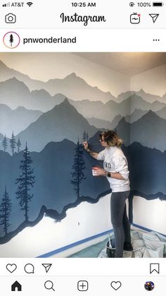 a woman is painting a mountain mural on the wall